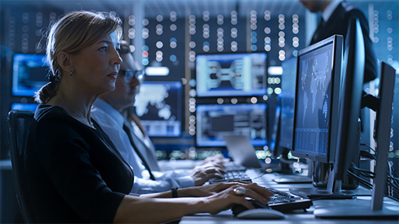 Line of analysts working on monitors to analyze data sit in a control room