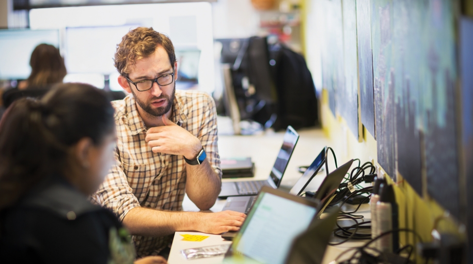 Two colleagues in a discussion as they collaborate on multiple laptops
