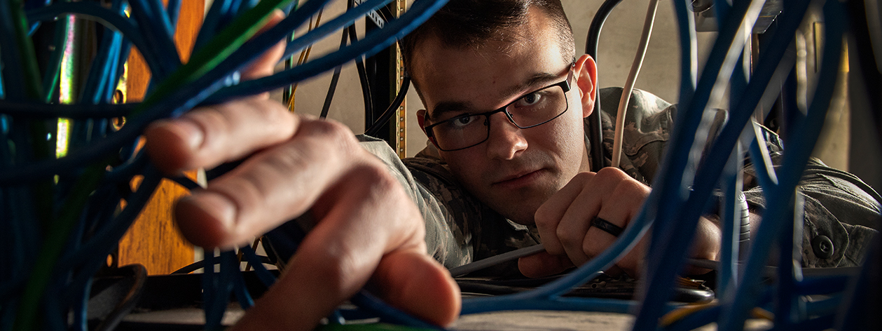 An Air Force man reaching through wires under a desk