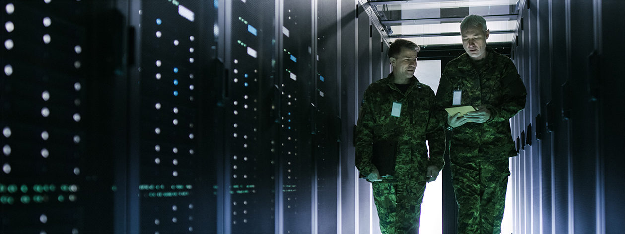 Two men in military uniform walk along a rack of servers