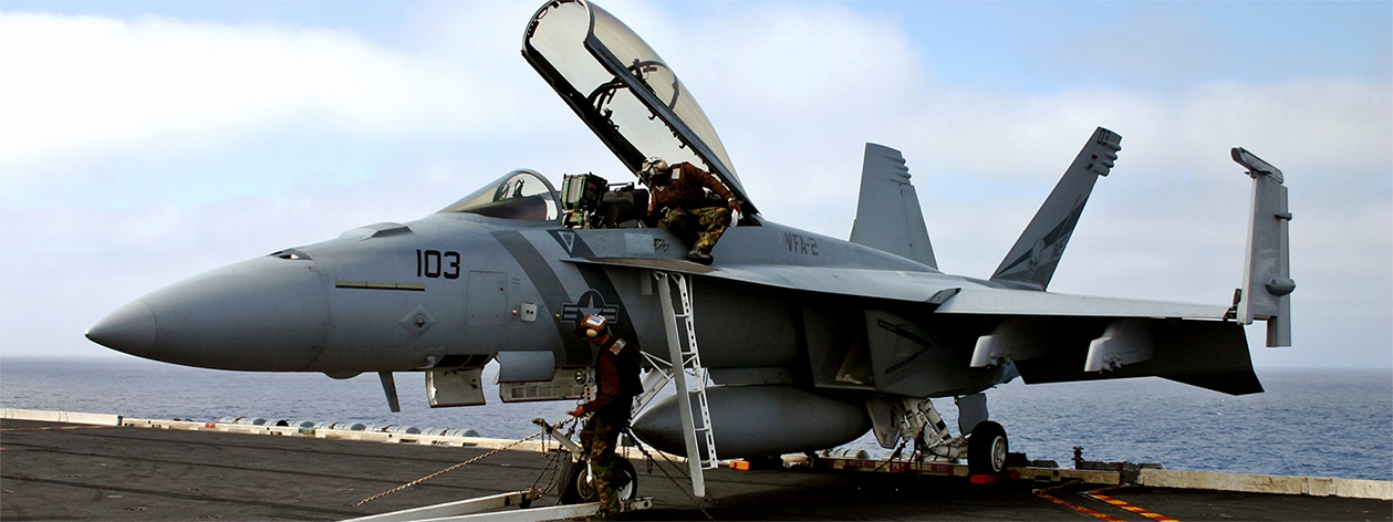 Serviceman walks under a fighter jet on the top of an aircraft carrier