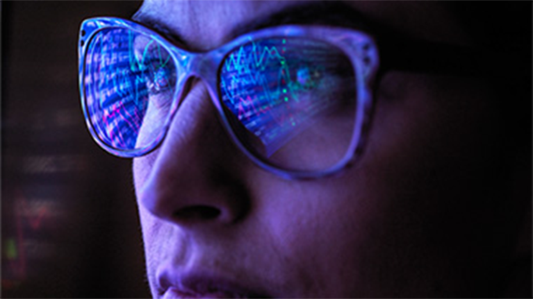 Zoomed in photo of a woman wearing glasses with a computer screen reflected in her lenses