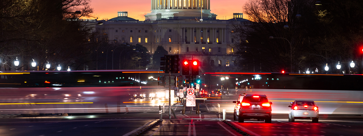 cars driving down Pennsylvania Ave at night towards the U.S. Capitol.